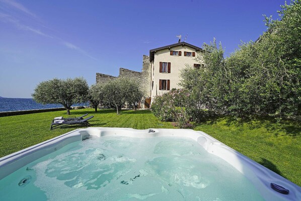 A hot tub in a grassy area with a view of a building and the sea.
