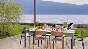 Un espace de restauration en plein air avec une table dressée pour quatre personnes, offrant une vue sur un lac et des montagnes en arrière-plan.