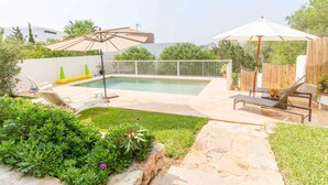 Patio con piscina, sillas de descanso y sombrillas.