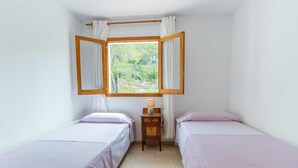 Una habitación pequeña y limpia con dos camas, una ventana con cortinas y una mesita de noche con lámpara.
