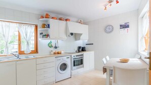 Una cocina compacta con muebles blancos, lavadora, horno y comedor con mesa y sillas.