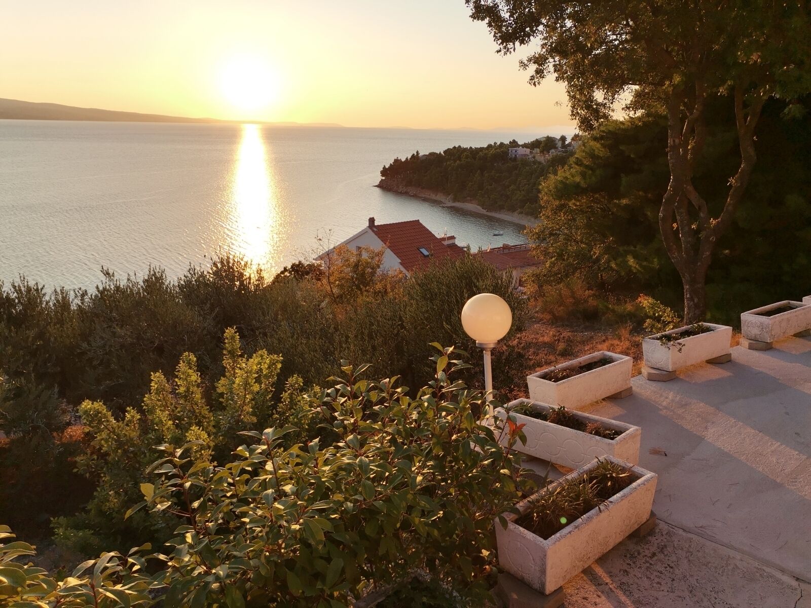 A coastal view with a sunset, a lamp post, and planters.