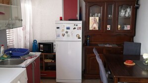 Ett kompakt kök med tvättmaskin, kylskåp, mikrovågsugn och en matplats med bord och stolar.