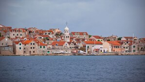 Un pueblo costero con edificios históricos de piedra, una iglesia blanca destacada con cúpula y un mar tranquilo.
