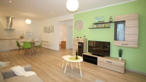 A modern living room with a green accent wall, a dining area with green chairs, a TV, and a fireplace.