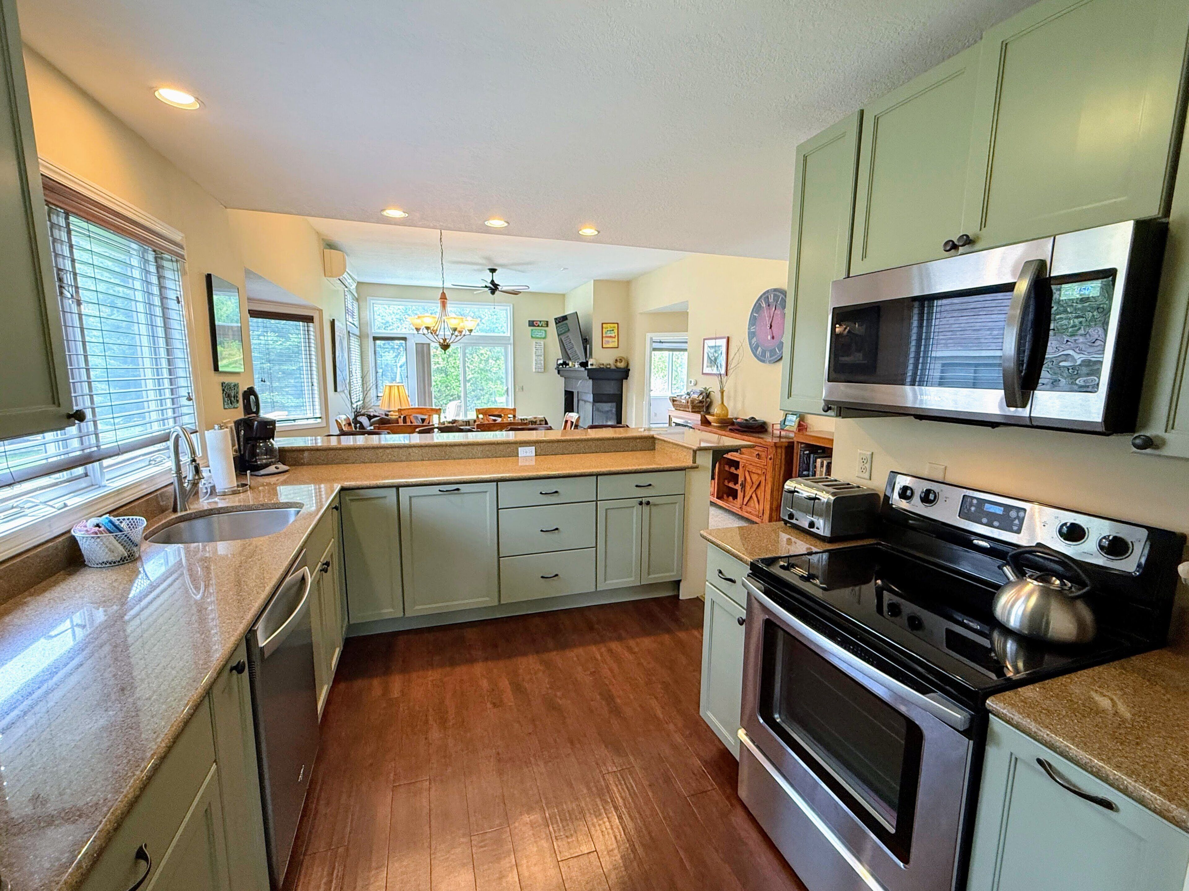 A kitchen with a central island, stainless steel appliances, and light green cabinets.