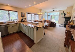 A kitchen with a central island, wooden cabinets, a sink, and a dining area with chairs and a table.
