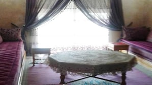 A room with a patterned rug, a round table with a lace tablecloth, a sofa, and a window with sheer curtains. - Nice apartment with pool access 4300 (Sidi Bouzid)