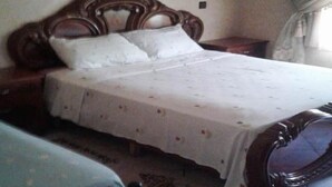 A bedroom with a wooden bed frame, white bedding, and a patterned rug. - Nice apartment with pool access 4300 (Sidi Bouzid)