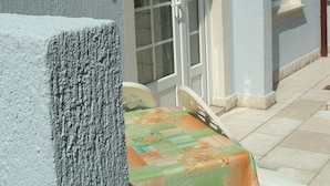 Un edificio con tetto in tegole, una porta con pannelli di vetro e un piccolo spazio esterno coperto con posti a sedere.