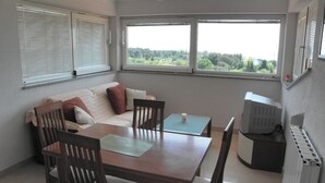 Un comedor con mesa, sillas, un sofá y vistas a zonas verdes a través de amplios ventanales.