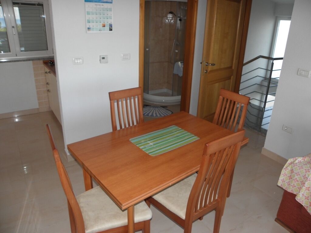 A dining area with a wooden table and chairs, a calendar on the wall, and a shower visible through a glass door.
