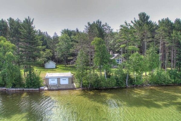 A lakeside property with a small dock, a shed, and a house surrounded by dense forest.
