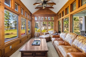 A room with large windows, a ceiling fan, a wooden table, and a leather sofa.