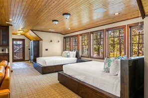 A bedroom with two beds, wooden ceiling, large windows, and a view of trees.