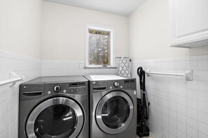A laundry room with two front-loading washing machines, a window, and a towel rack.