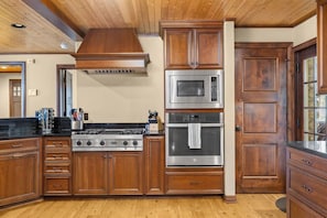 A kitchen with wooden cabinets, a stainless steel oven, and a microwave. - The Stone House  | Premier West Twin Lake Home (Lewiston)
