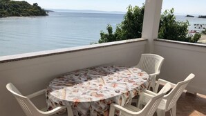 Een ronde tafel met een bloemrijk tafelkleed en vier witte stoelen op een balkon met uitzicht op zee.
