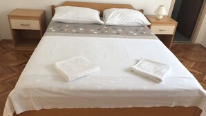 Een net opgemaakt bed met witte lakens en twee gevouwen handdoeken.