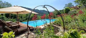 Un espace piscine agrémenté de chaises longues et d’un parasol, entouré d’une végétation luxuriante et dominé par une chaîne de montagnes.