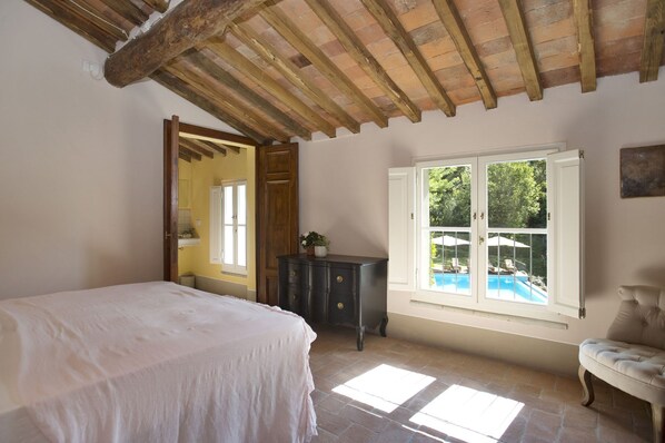 Une chambre avec un lit, une commode, une fenêtre donnant sur une piscine et un banc.