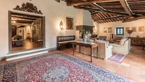 A spacious living room with a high wooden ceiling, a large ornate mirror, and a traditional fireplace.