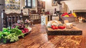 A rustic kitchen with a wooden table displaying bread, cheese, tomatoes, and artichokes.