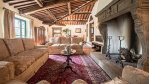 A spacious living room with a high wooden ceiling, a fireplace, and a traditional rug.