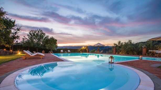 A swimming pool with lounge chairs and a hot tub, surrounded by a brick patio and trees.