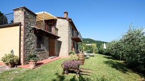 A stone house with a balcony, a garden with a wheelbarrow of flowers, and a clear blue sky. - Villa in Lisciano Niccone with 5 bedrooms sleeps 10 (Lisciano Niccone)