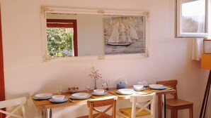 Uma área de refeições com uma mesa posta para quatro pessoas, um quadro de um veleiro e uma janela com vista para árvores.