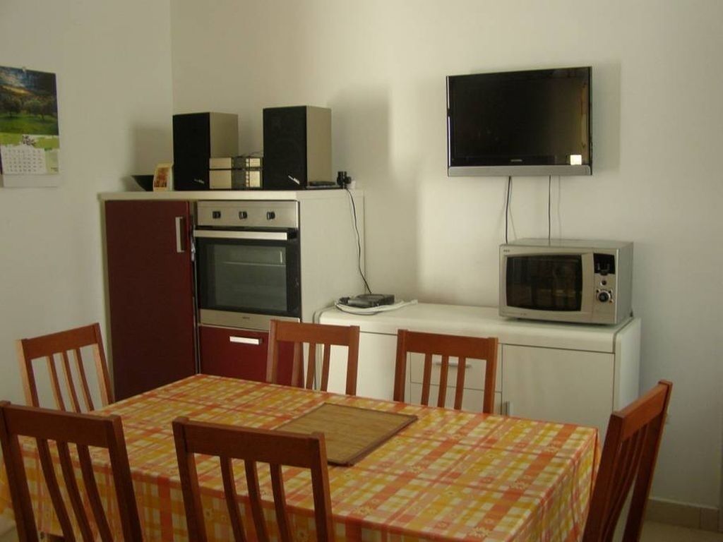 Une cuisine compacte équipée d’un four à micro-ondes, d’un four et de deux haut-parleurs placés sur un meuble. Une table à manger avec des chaises se trouve devant la cuisine.