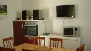 A compact kitchen with a microwave, oven, and two speakers on a cabinet. A dining table with chairs is in front of the kitchen. - Holiday Home in Preko with Seaview, Terrace, Air condition, WIFI (4571-1) (Preko)