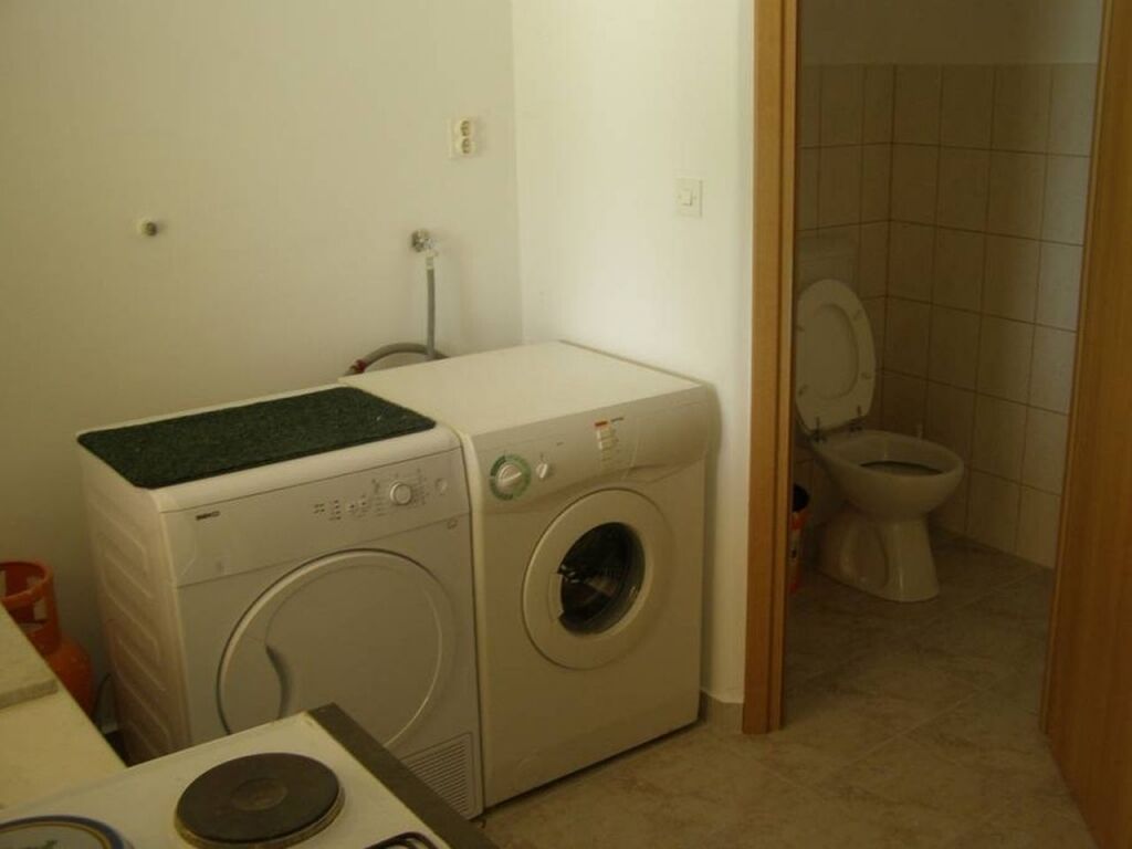 A laundry area with a washing machine and dryer, a toilet, and a small table with a mat.