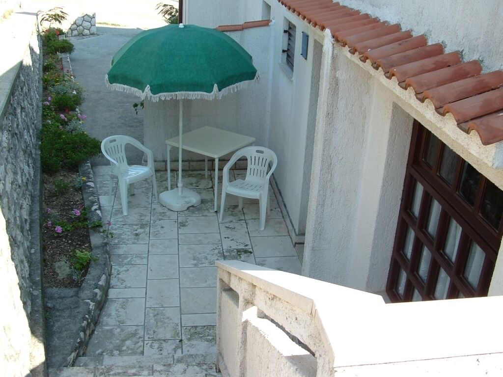 A small outdoor patio with a table and two chairs, a green umbrella, and a stone wall.