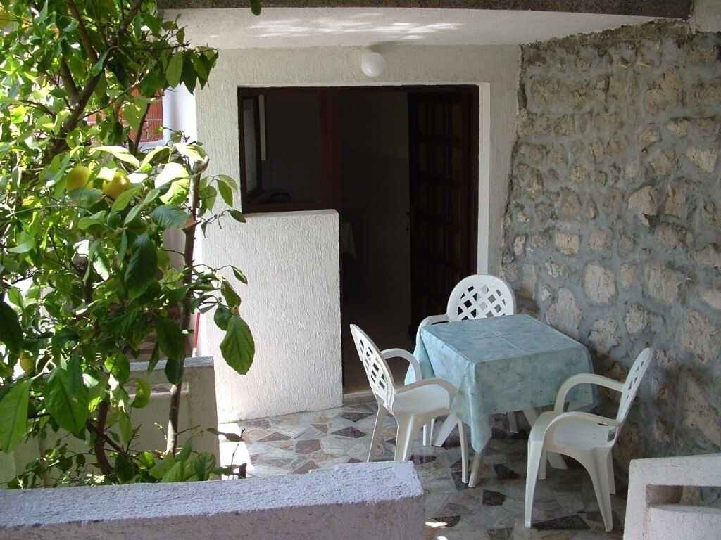 Eine Terrasse mit Tisch und Stühlen, eine Steinmauer und eine Tür, die in einen Innenraum führt.