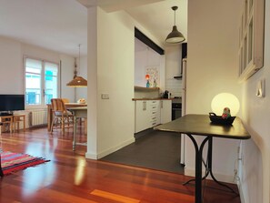 A modern kitchen with white cabinets, a dining area with a table and chairs, and a hallway with a rug.