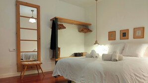 Un dormitorio con una cama, una escalera de madera, una lámpara colgante y un estante en la pared con ropa.