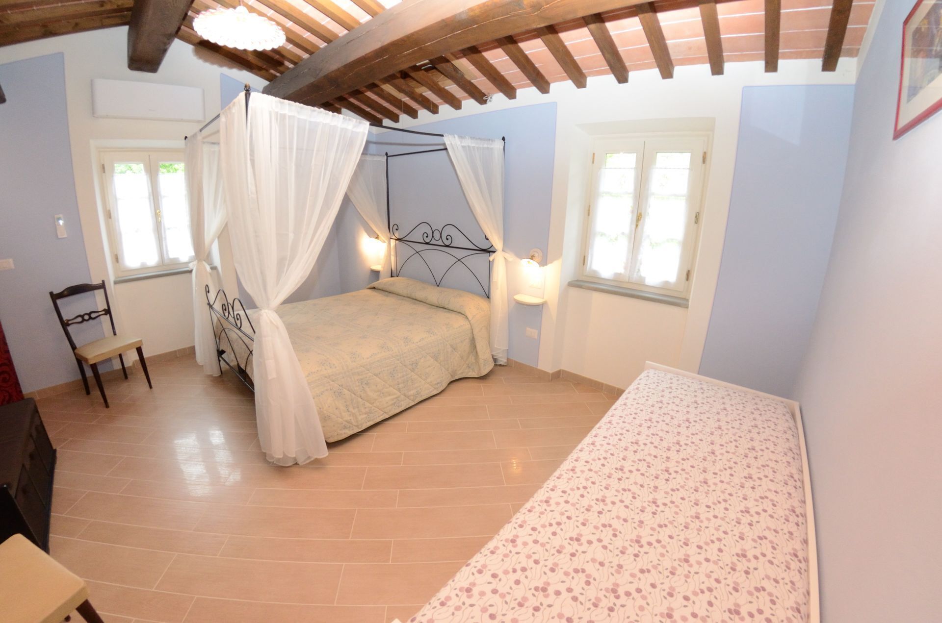 A bedroom with a bed under a canopy, a bedside table, a chair, and a window.