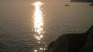 A calm sea with the sun reflecting on the water, a rocky shoreline, and a distant landmass.
