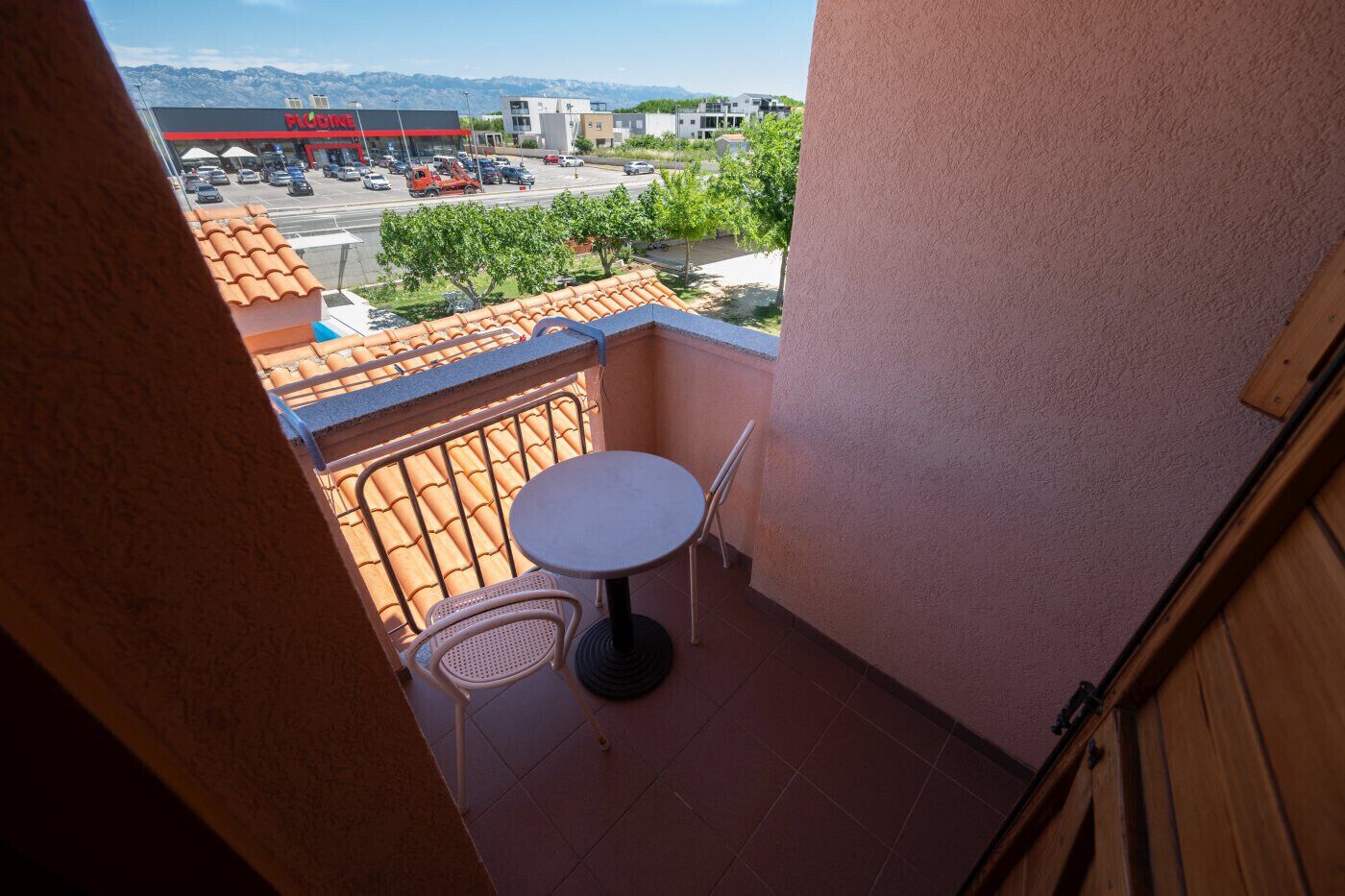 A balcony with a table and chairs, a tiled floor, and a view of a parking lot and buildings in the distance.