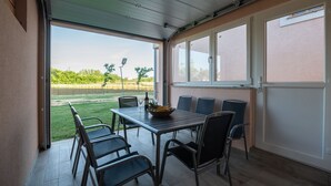 A covered patio with a table and chairs, a bottle of wine, and a bowl of fruit.