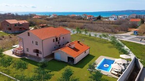 A large two-story house with a red-tiled roof, a swimming pool, and a view of the sea.
