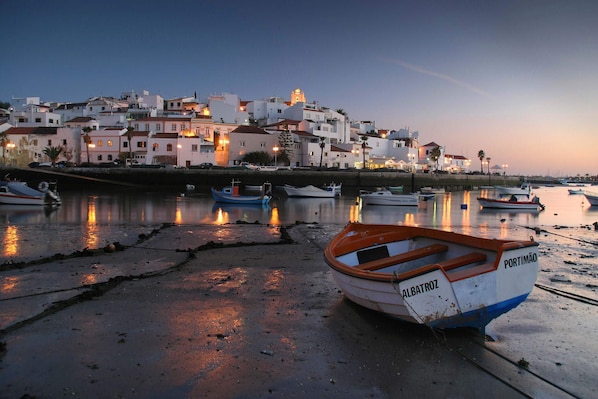 A coastal town with boats docked along the shore and buildings in the background. - Premier nº 45 - Modern Three Bedroom Apartment with Jacuzzi (Ferragudo)