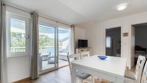 Una habitación moderna con una mesa blanca, sillas, un televisor y un balcón con mobiliario exterior.