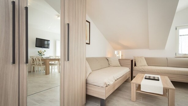 Ein modernes, helles Zimmer mit einer Couch, einem Couchtisch und einem an der Wand montierten Fernseher.