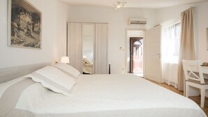 Ein Schlafzimmer mit einem großen Bett, einem Nachttisch, einem Sessel, einem Bild an der Wand und einer Tür zu einem weiteren Raum.