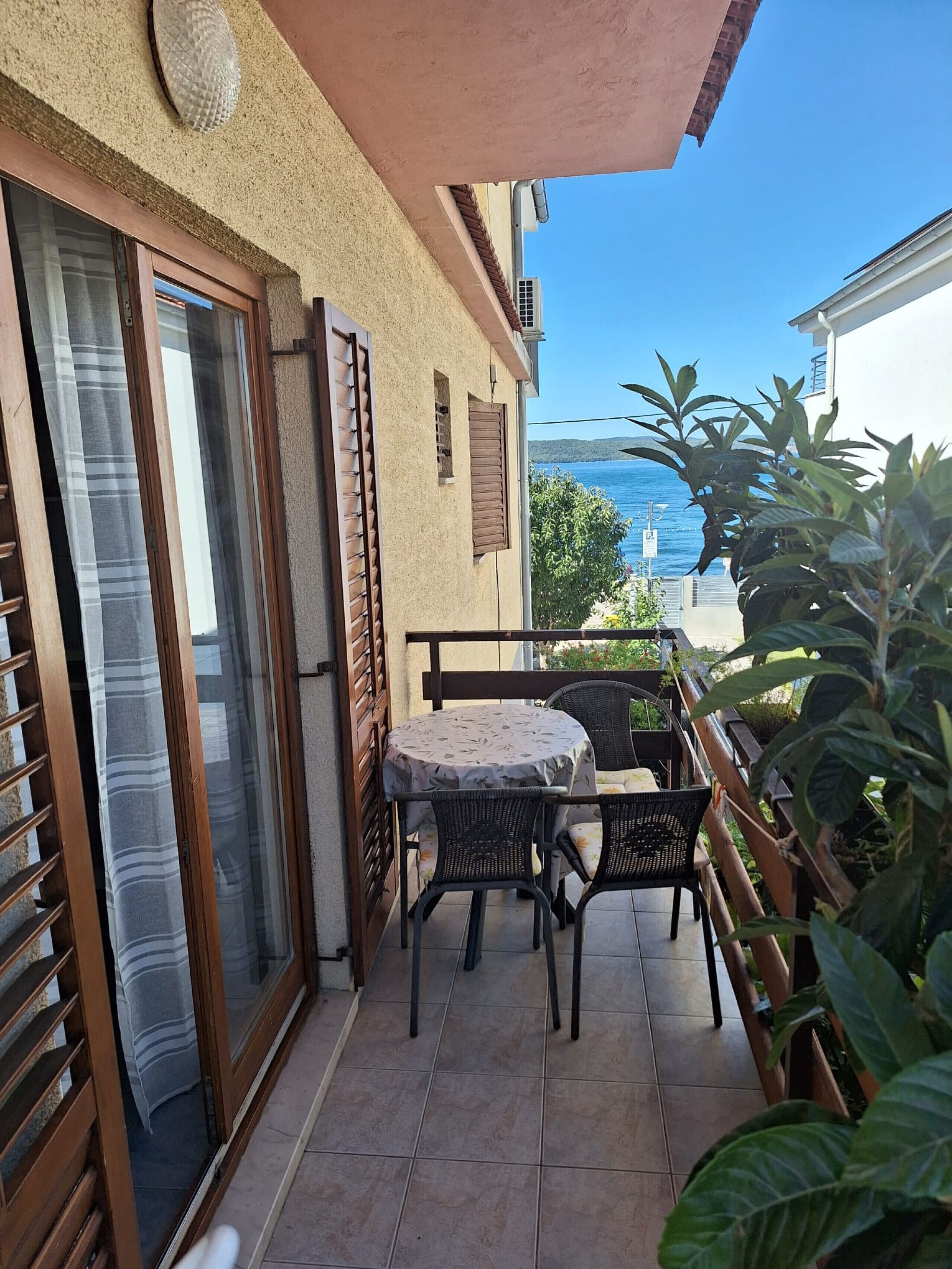 A balcony with a table and chairs, a sliding glass door, and a view of the sea.