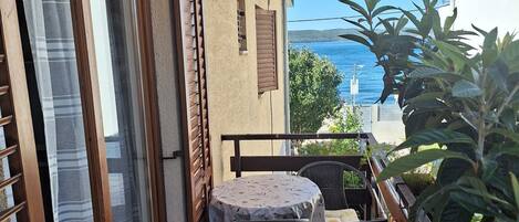 A balcony with a table and chairs, a sliding glass door, and a view of the sea.
