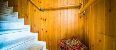 A wooden staircase with a handrail, white steps, and a wicker basket with dried flowers at the bottom.